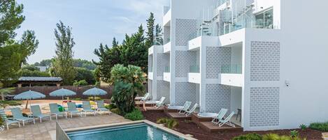A modern hotel with a pool area, sun loungers, and a clear sky.