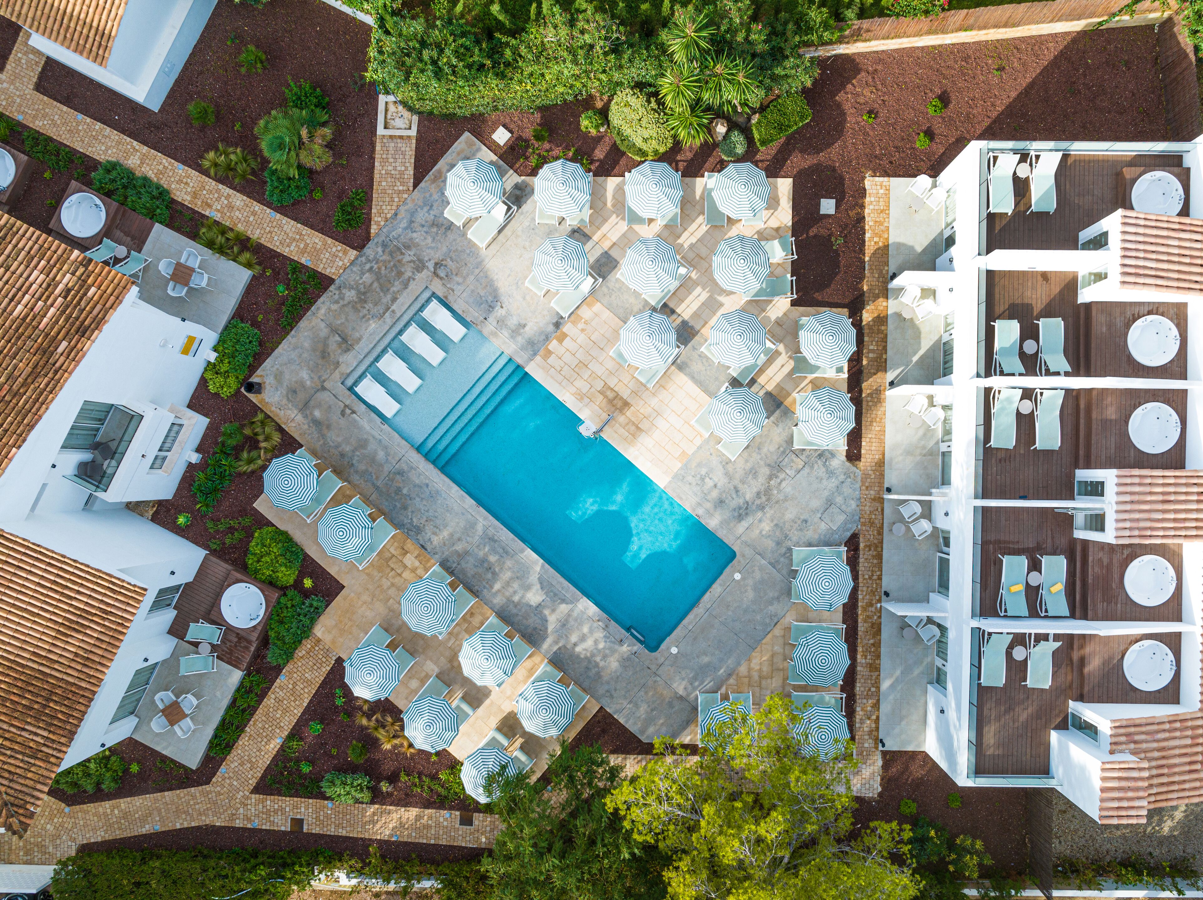 Vue aérienne d’un complexe hôtelier doté d’une piscine centrale, entourée d’espaces de détente avec des parasols, d’une terrasse avec des sièges et d’un bar au bord de la piscine.