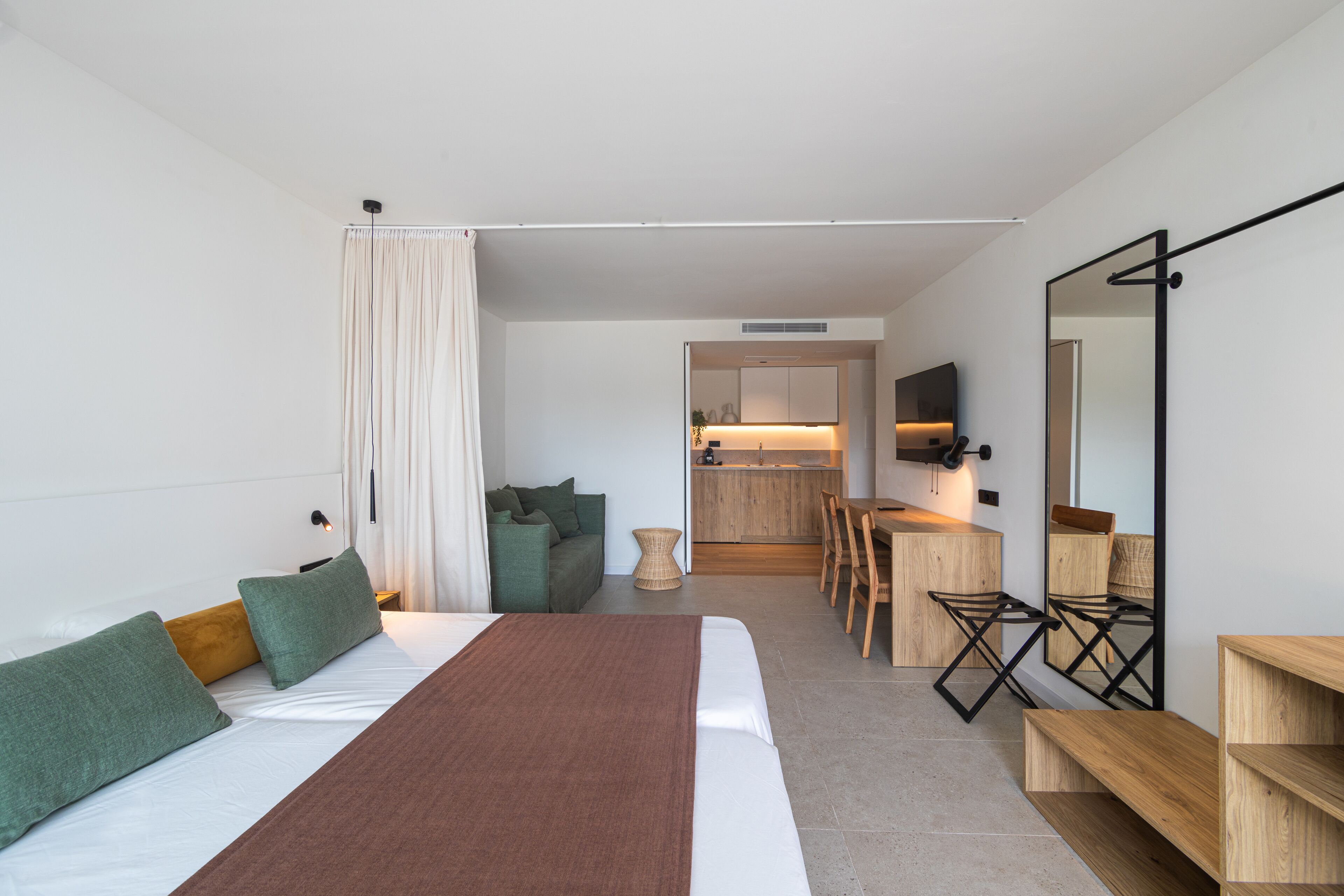 Ein modernes Hotelzimmer mit einem großen Bett, einem Essbereich und einer Küche im Hintergrund.