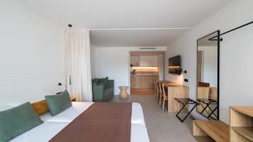 Una habitación de hotel moderna con una cama grande, una zona de comedor y una cocina al fondo.