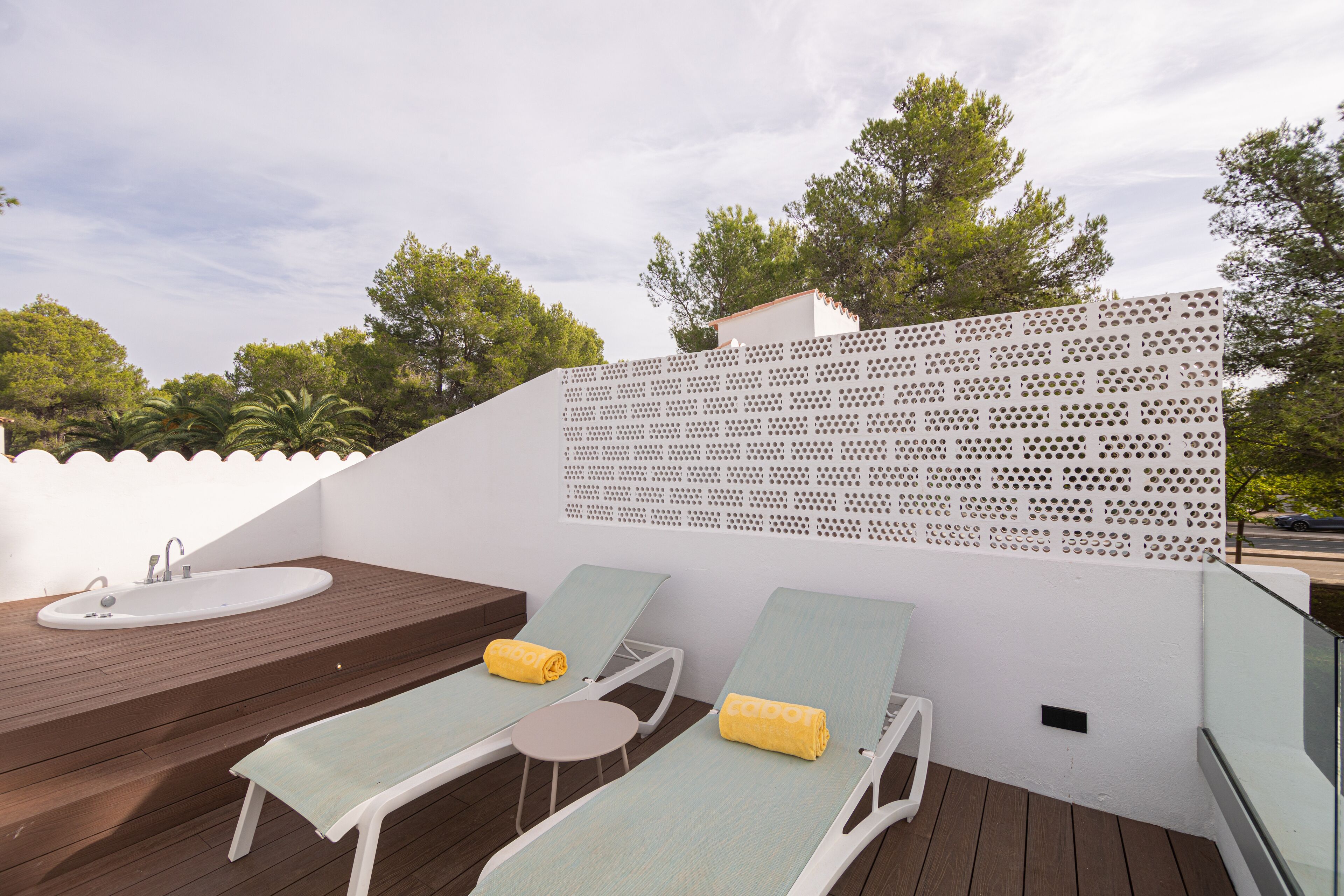 A rooftop terrace with a wooden deck, two lounge chairs with towels, a white sink, and a perforated privacy screen.