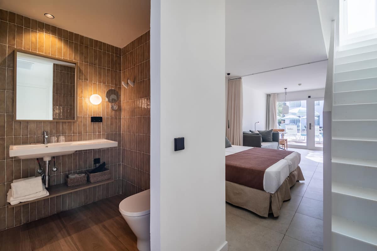A modern bathroom with a large sink, mirror, and toilet. The room features a wooden floor and a large window.