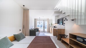 A modern hotel room with a sofa, a long rug, a desk, and a TV mounted on the wall.
