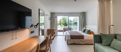 Habitación de hotel moderna con escritorio de madera, cama con ropa de cama verde, sofá verde y vistas a una piscina y jardín.