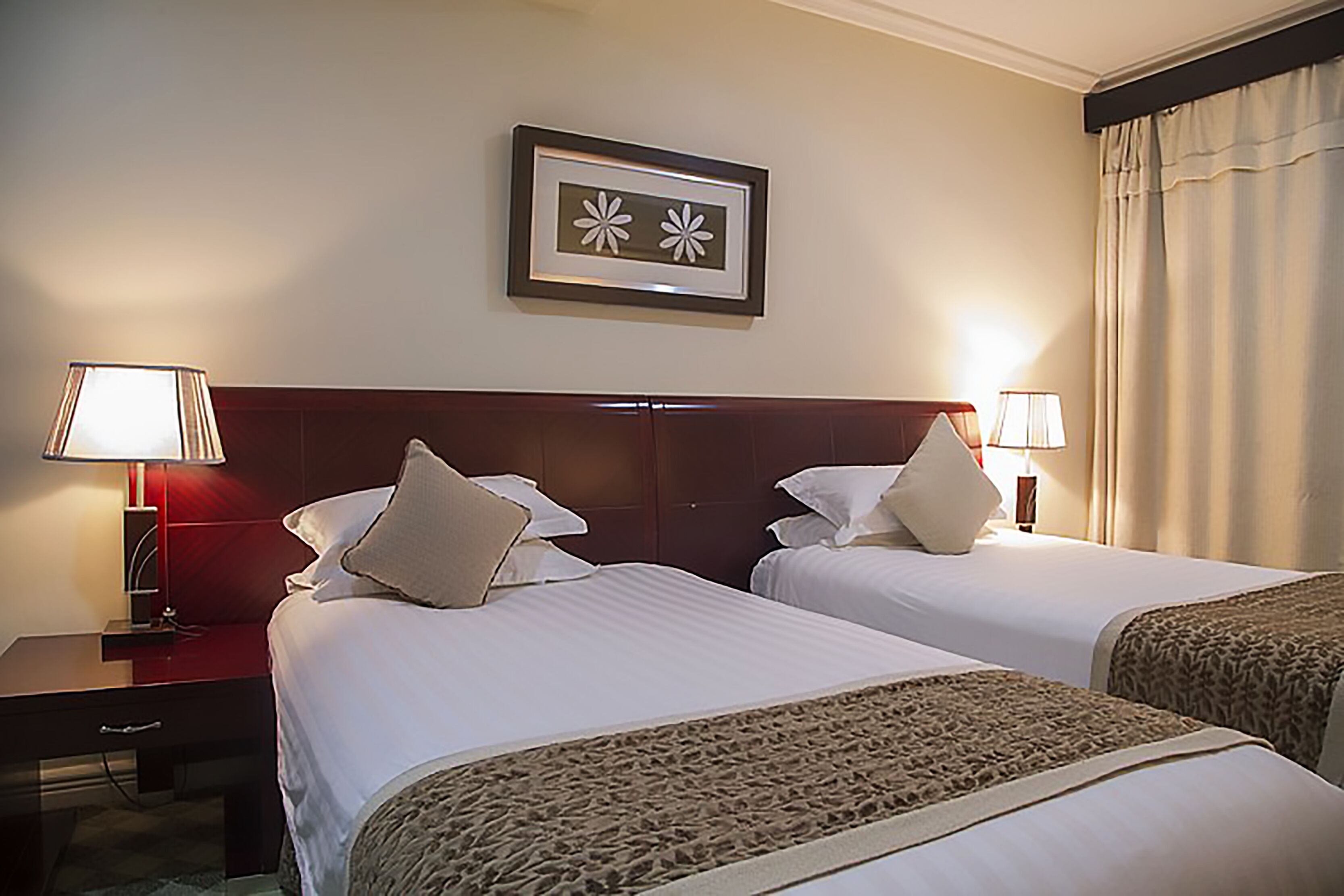 A hotel room with two beds, a nightstand, a lamp, and a framed picture on the wall.