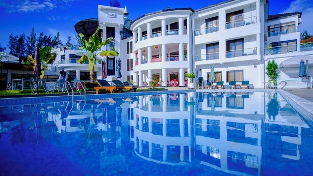 A modern hotel with a central pool, multiple balconies, and a clear blue sky.