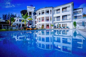 A modern hotel with a central pool, multiple balconies, and a clear blue sky.