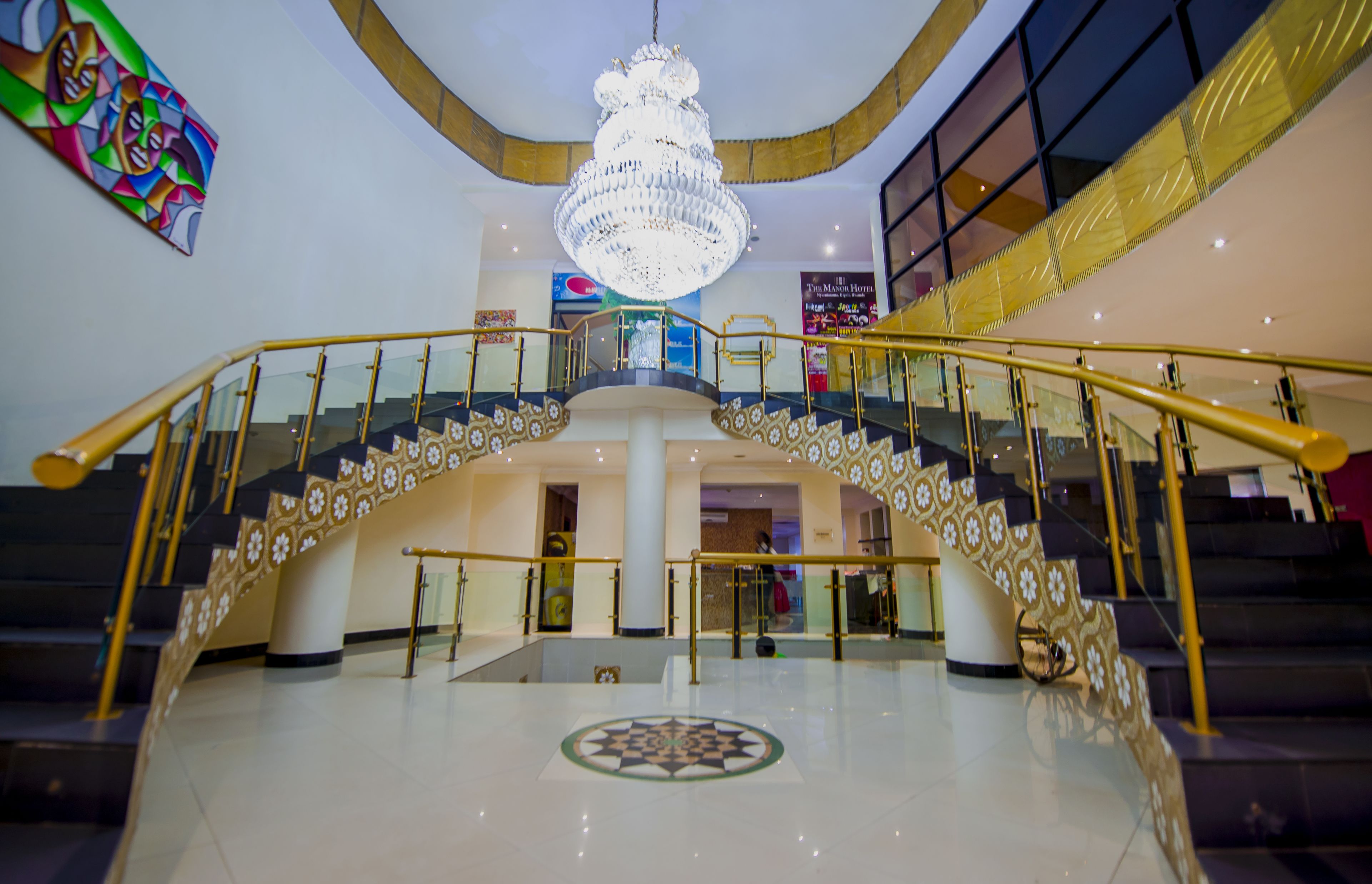 A grand staircase with ornate railings and a chandelier, leading to an upper level in a modern building.