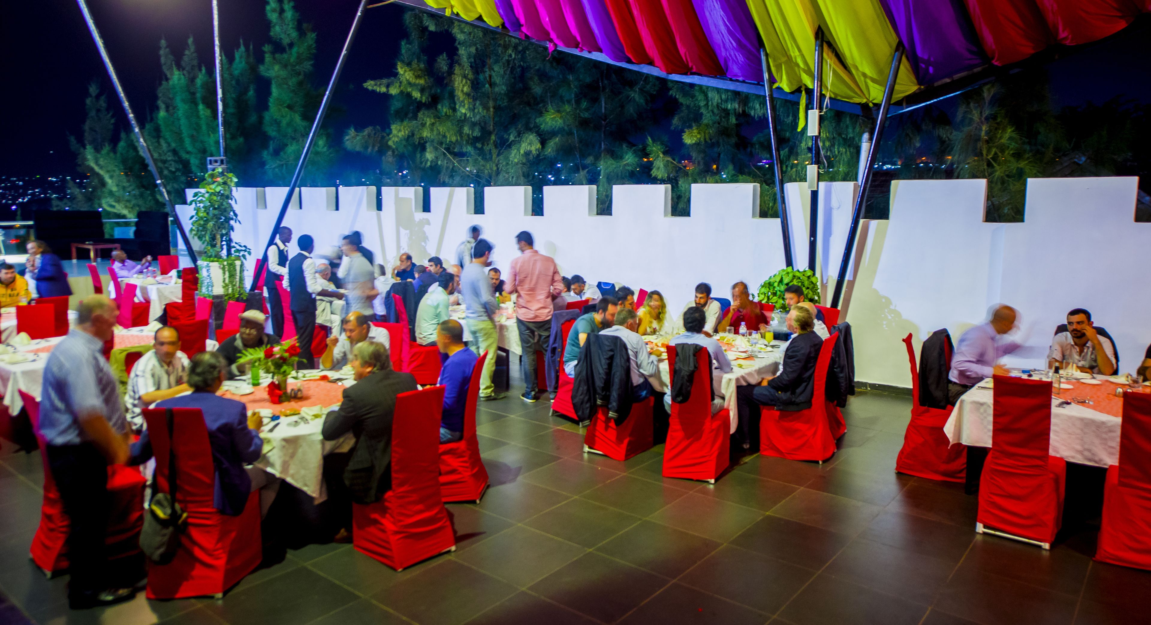 Un salón de banquetes con mesas redondas y sillas rojas, preparado para un evento formal.