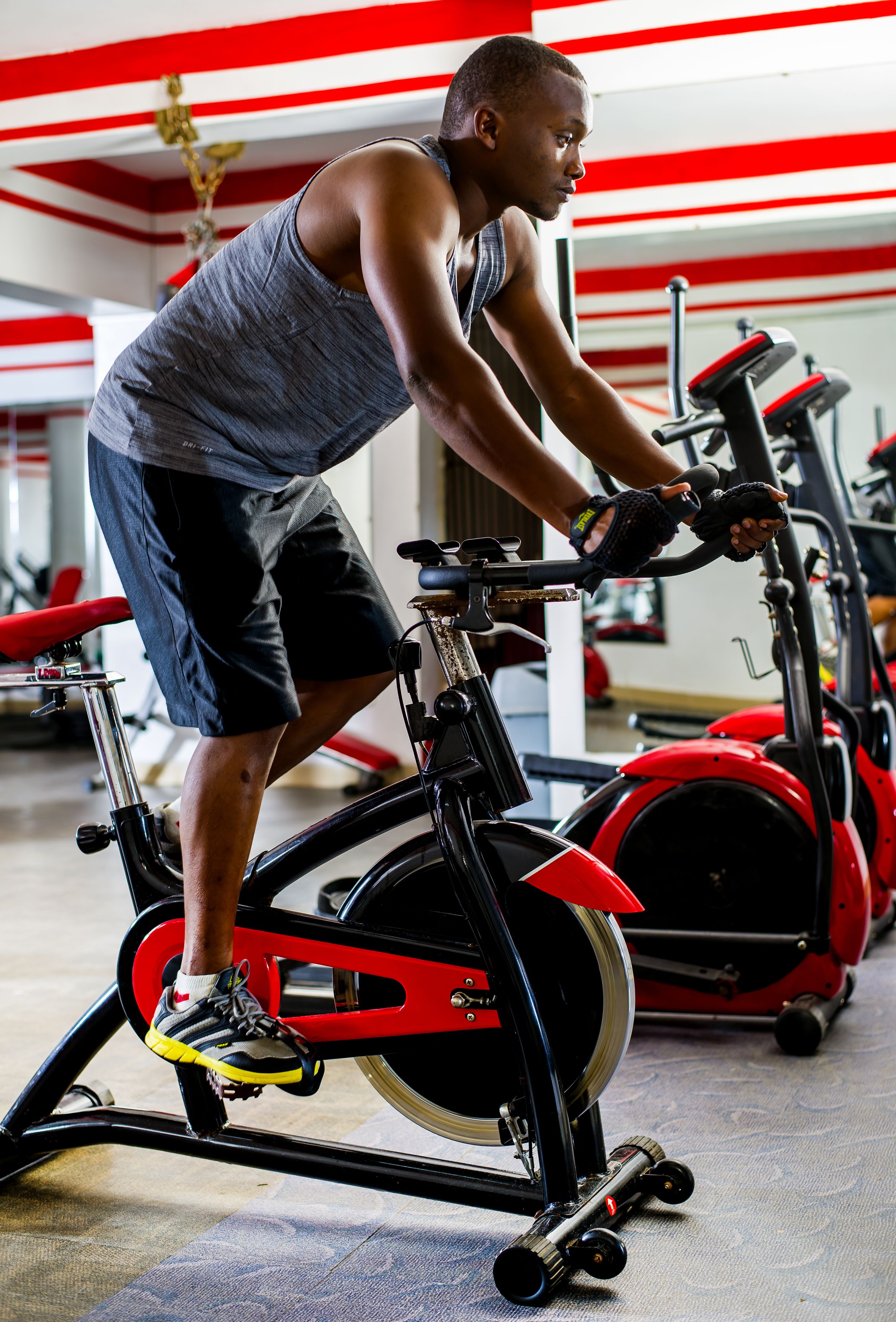 A person using a stationary bike in a gym with red and white striped walls.