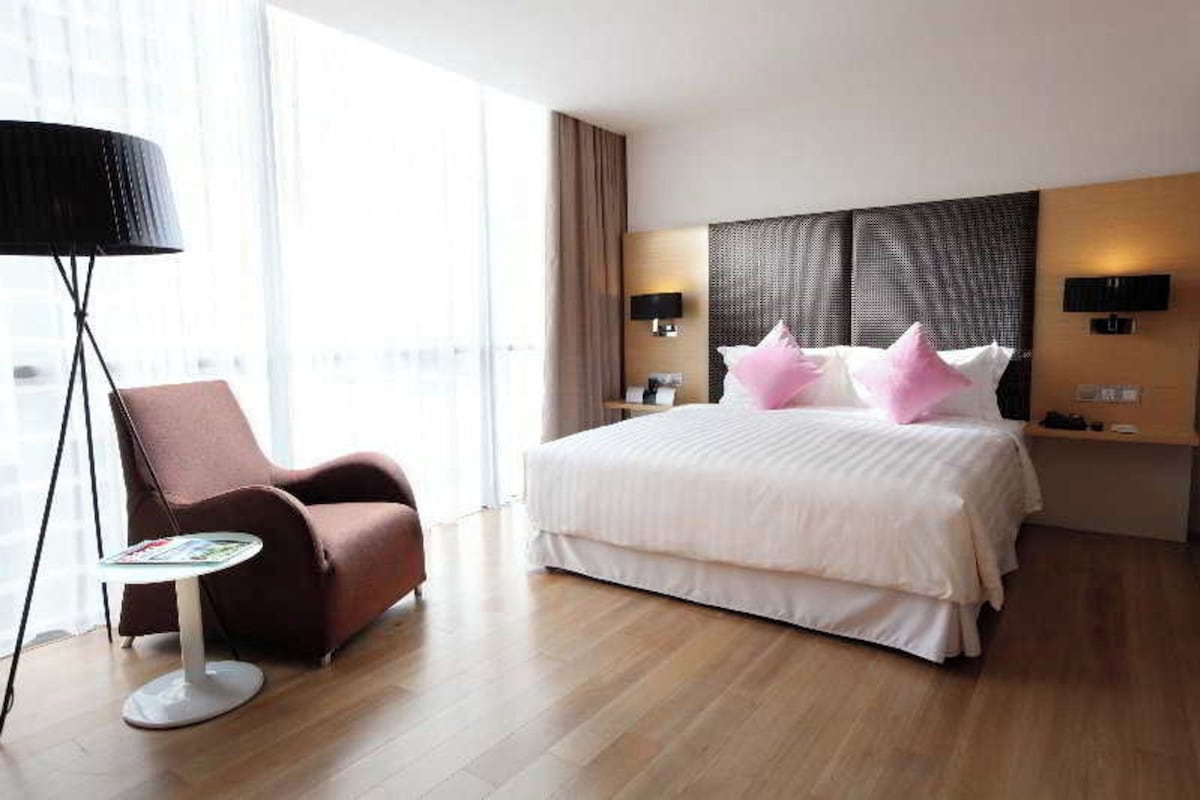 A hotel room with a large bed, a chair, a table, and a lamp.