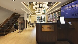 A reception area with a wooden reception desk labeled "VERSÓ RÉCEPTION," a staircase, and a wall with a large sign reading "VERSÓ HOTEL BOUTIQUE." - Hôtel Versō (Magog)