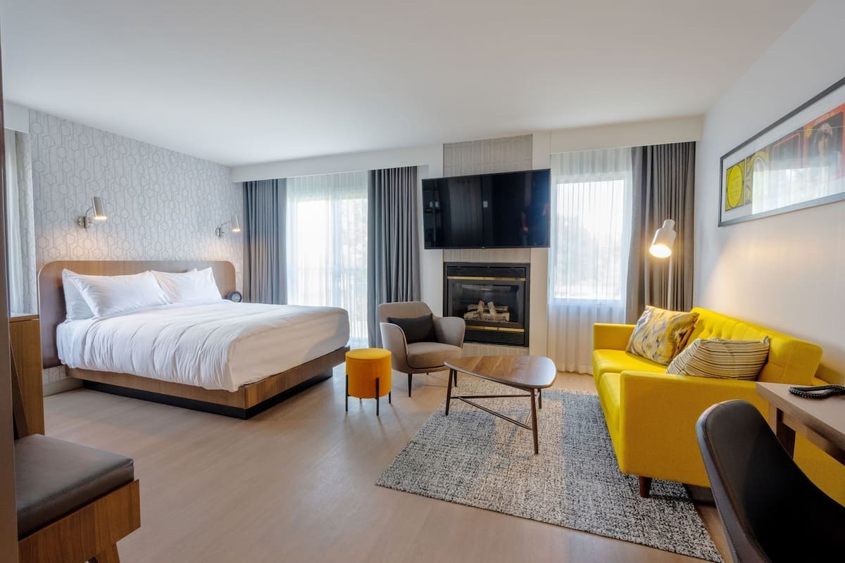 A hotel room with a bed, a sofa, a chair, a TV, and a fireplace.