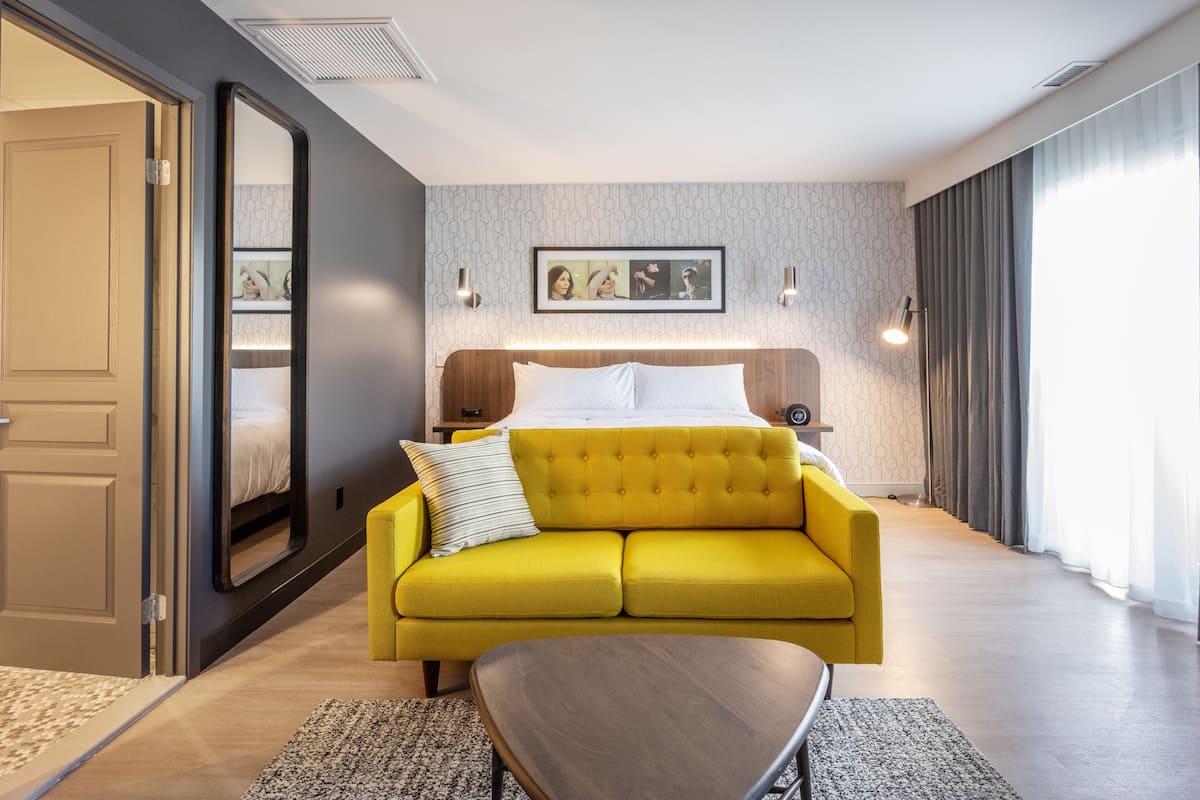 A hotel room with a bed, a yellow sofa, a wooden coffee table, and a framed picture on the wall.