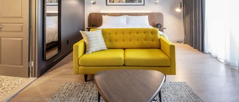 A hotel room with a bed, a yellow sofa, a wooden coffee table, and a framed picture on the wall.