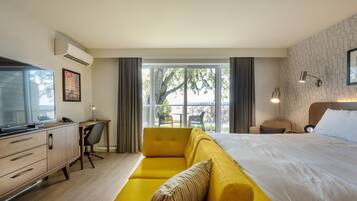 Habitación de hotel moderna con una cama grande, un sofá amarillo, un escritorio con una computadora y vistas al exterior.