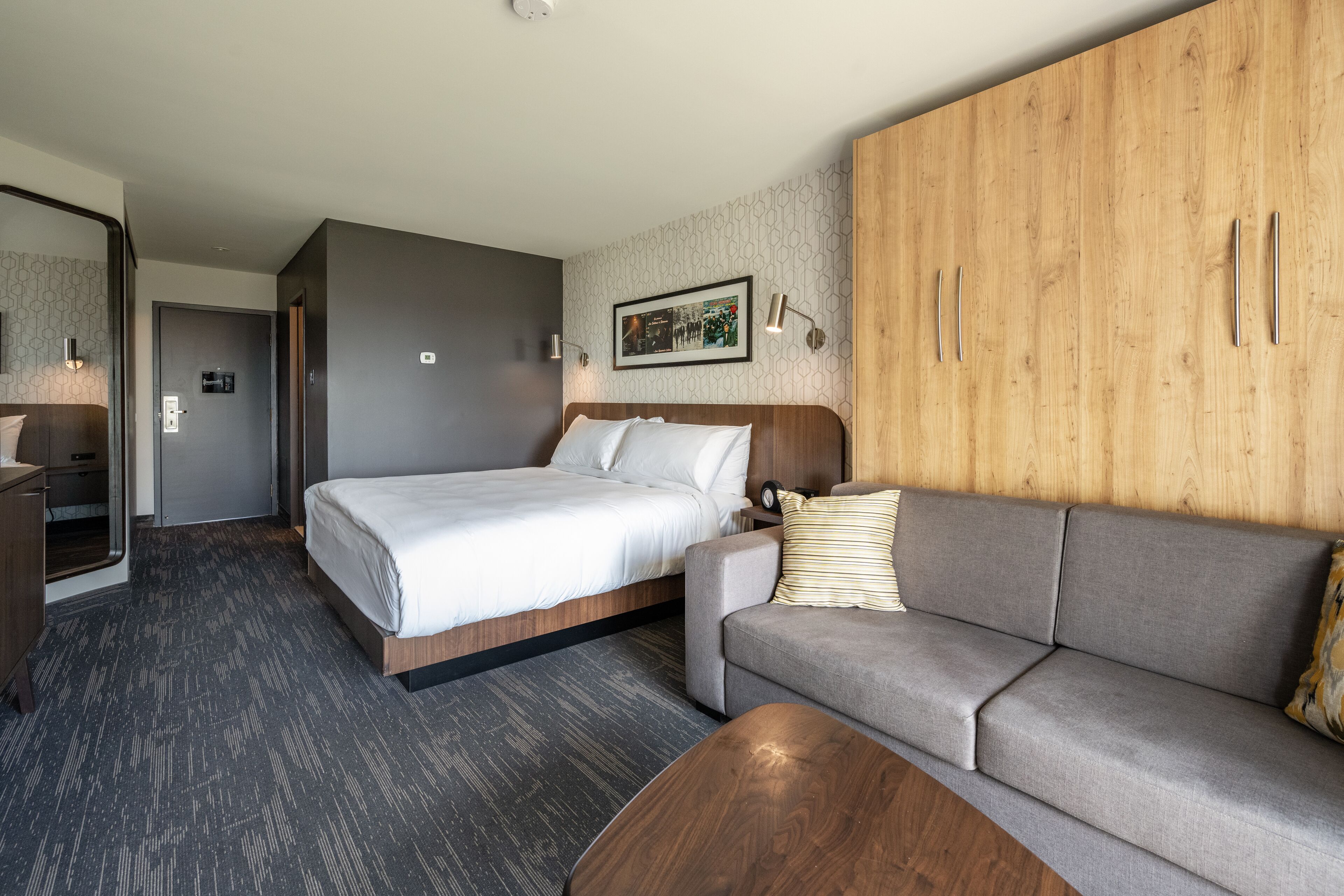A hotel room with a bed, a sofa, a wooden wardrobe, and a mirror.