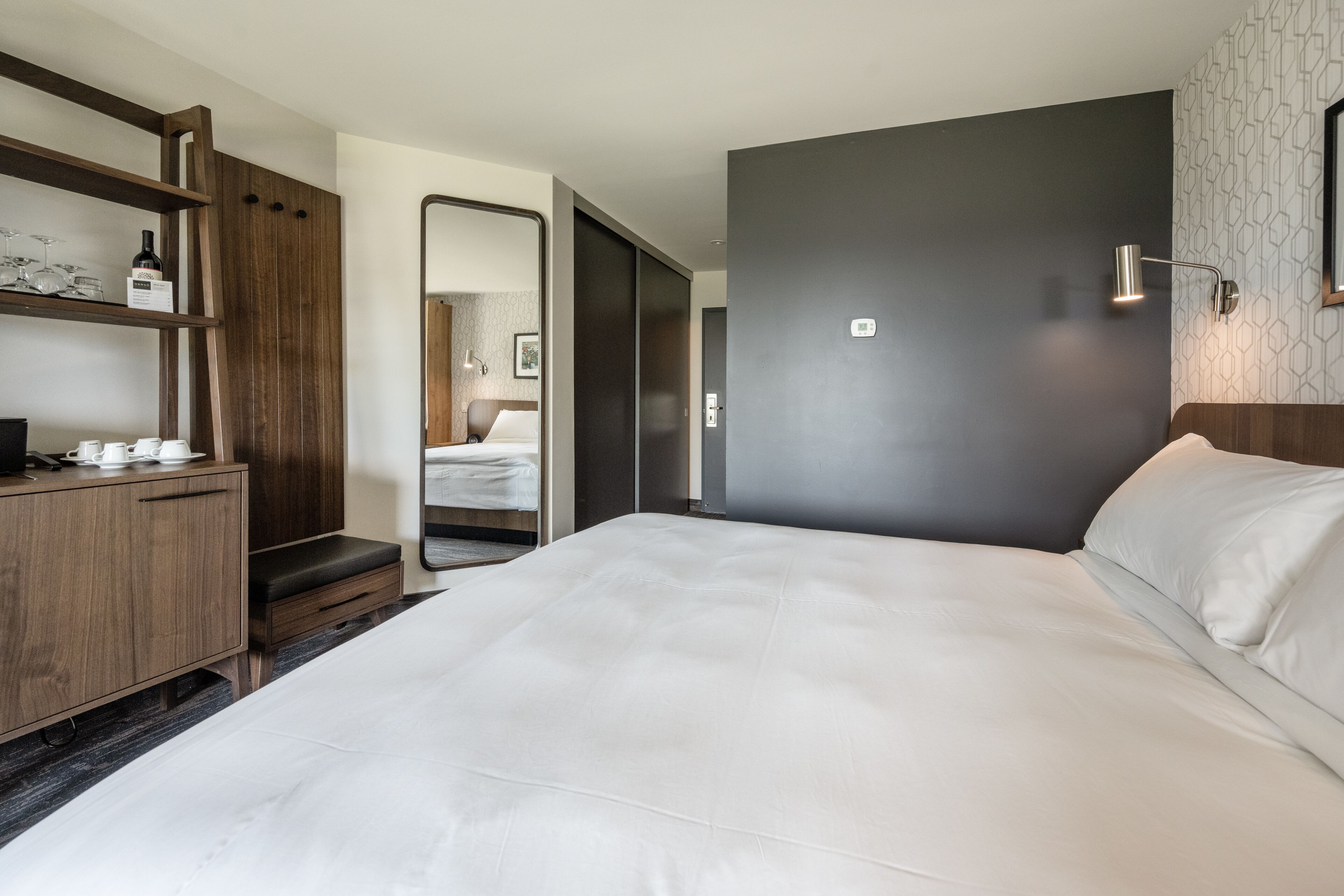 Ein modernes Hotelzimmer mit einem großen Bett, Holzmöbeln, einem Spiegel und einer Wandleuchte.