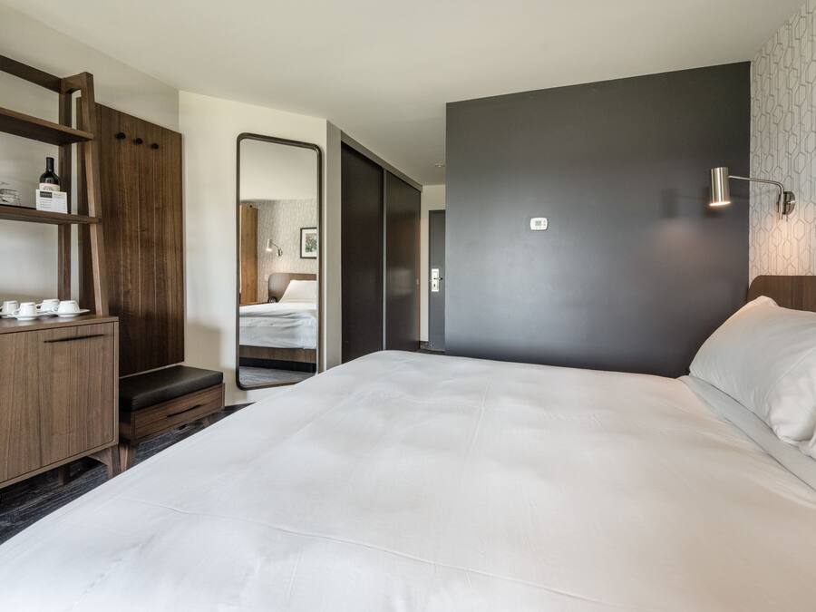 Ein modernes Hotelzimmer mit einem großen Bett, Holzmöbeln, einem Spiegel und einer Wandleuchte.