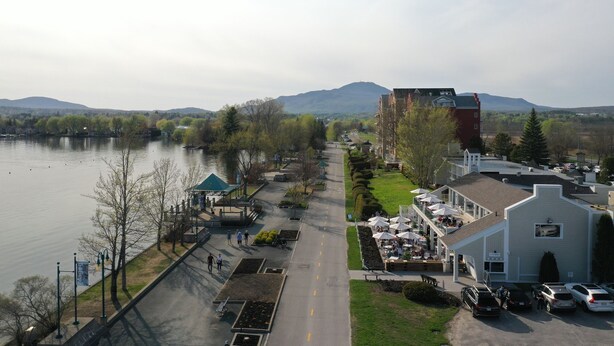 A lakeside view with a pedestrian path, a gazebo, and a building with outdoor seating.