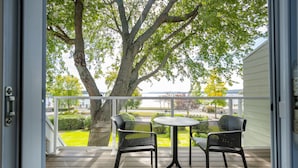 A balcony with a table and two chairs, overlooking a grassy area and a body of water. - Hôtel Versō (Magog)