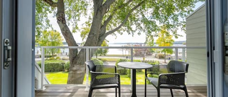 Un balcon avec une table et deux chaises, donnant sur une zone herbeuse et un plan d’eau.