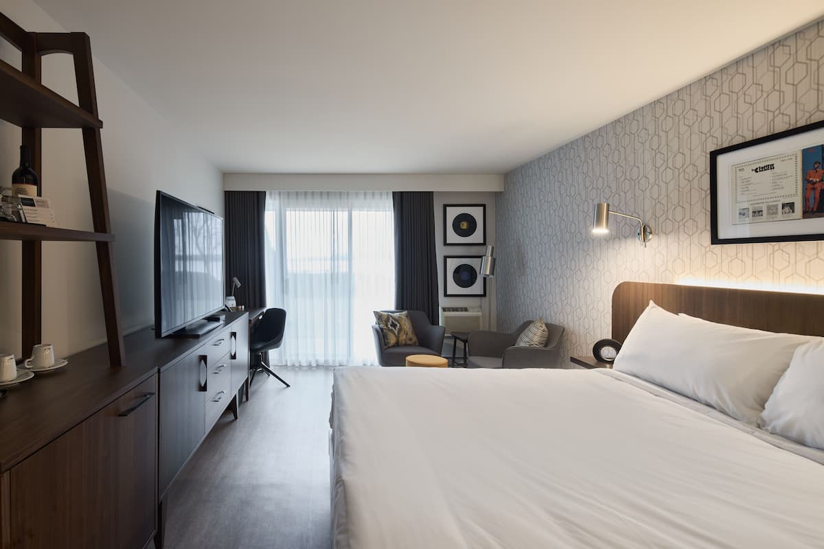A hotel room with a large bed, a desk with a chair, a sofa, a TV, and a wardrobe.