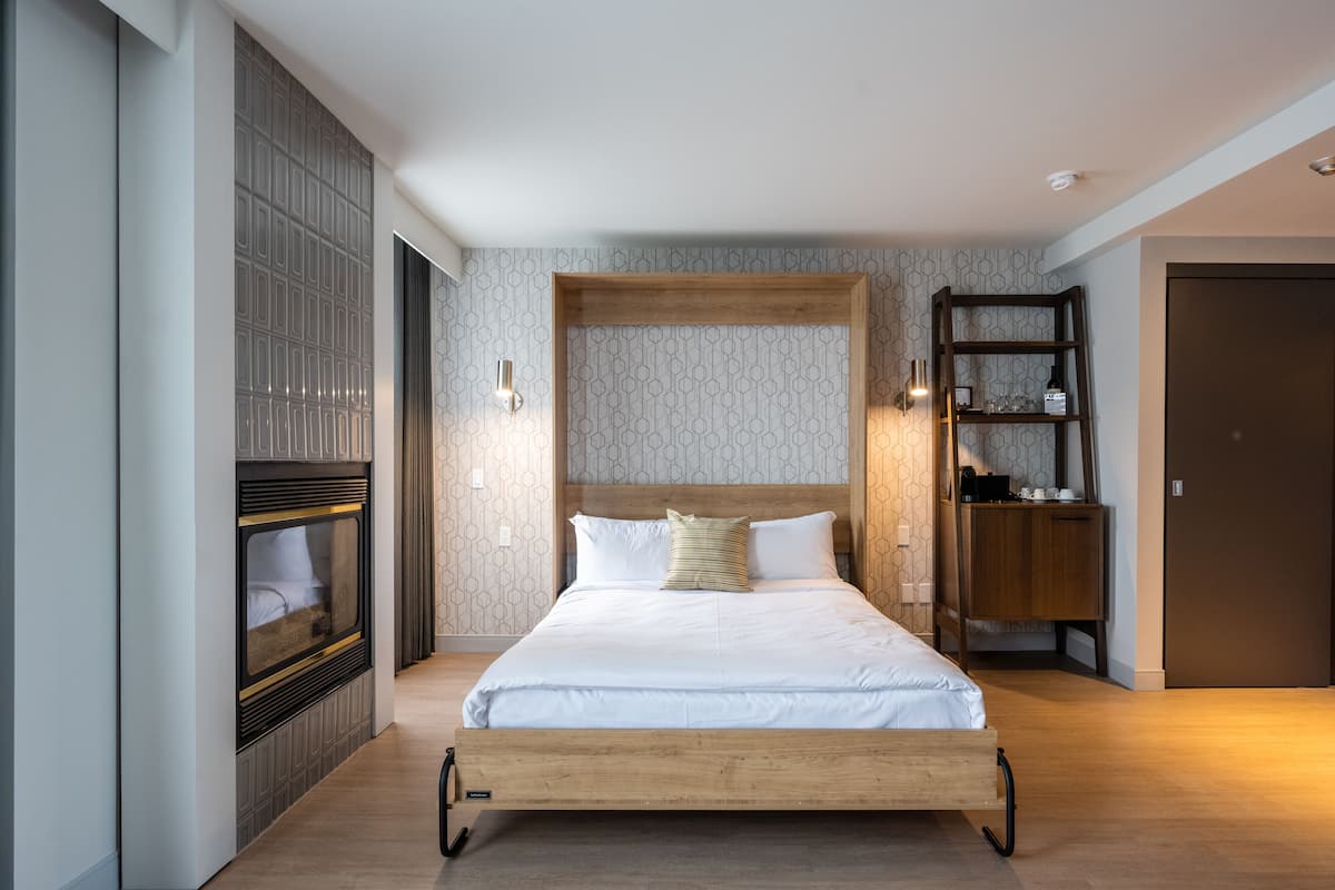 A modern bedroom with a wooden bed frame, a built-in fireplace, and a wooden shelving unit.
