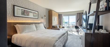 A modern hotel room with a large bed, a desk, a chair, and a balcony with a view.