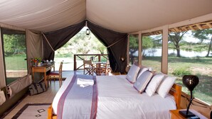 Ein Zeltraum mit einem Bett, einem Schreibtisch und einem Stuhl. Blick auf einen See und Bäume.
