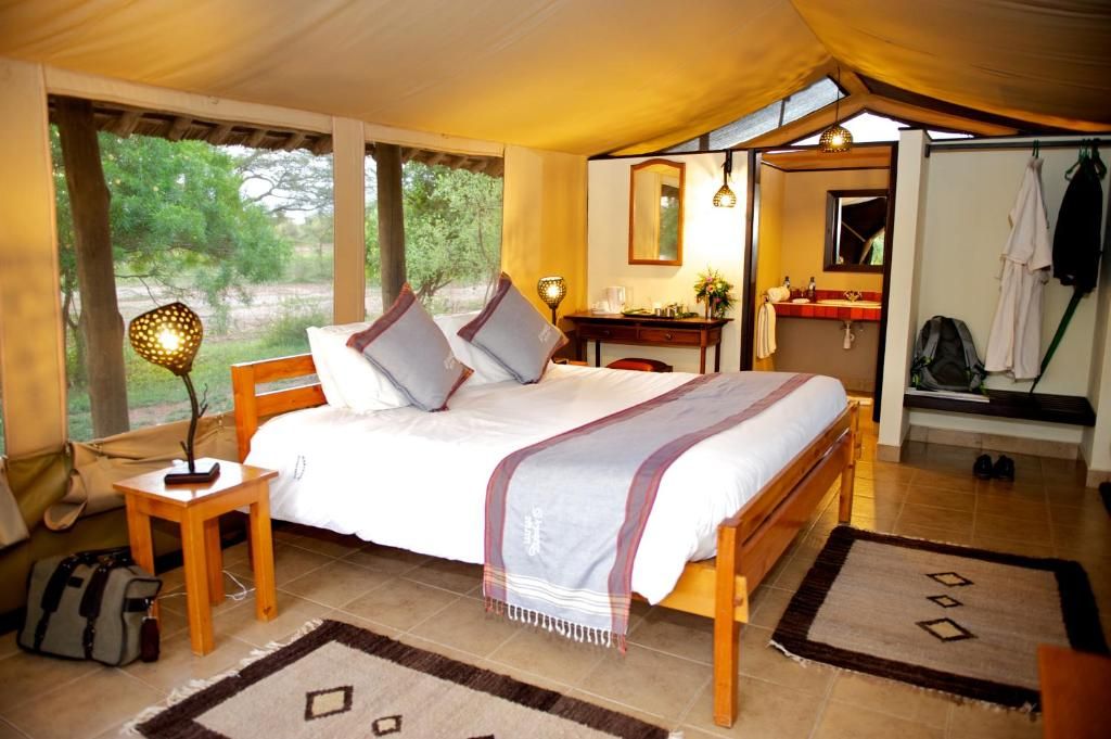 A tented accommodation room with a bed, bedside table, lamp, and a view of the outdoors.