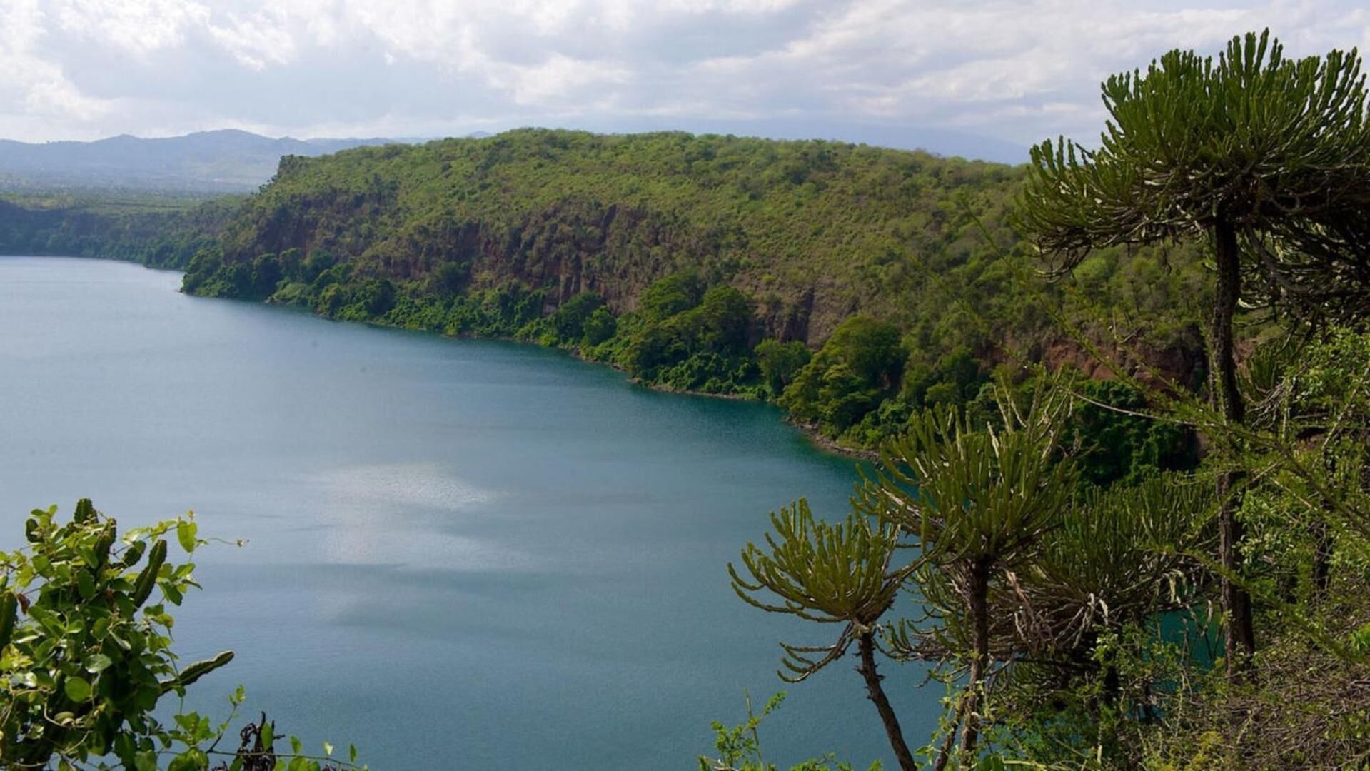 Vista de um lago rodeado por colinas arborizadas.