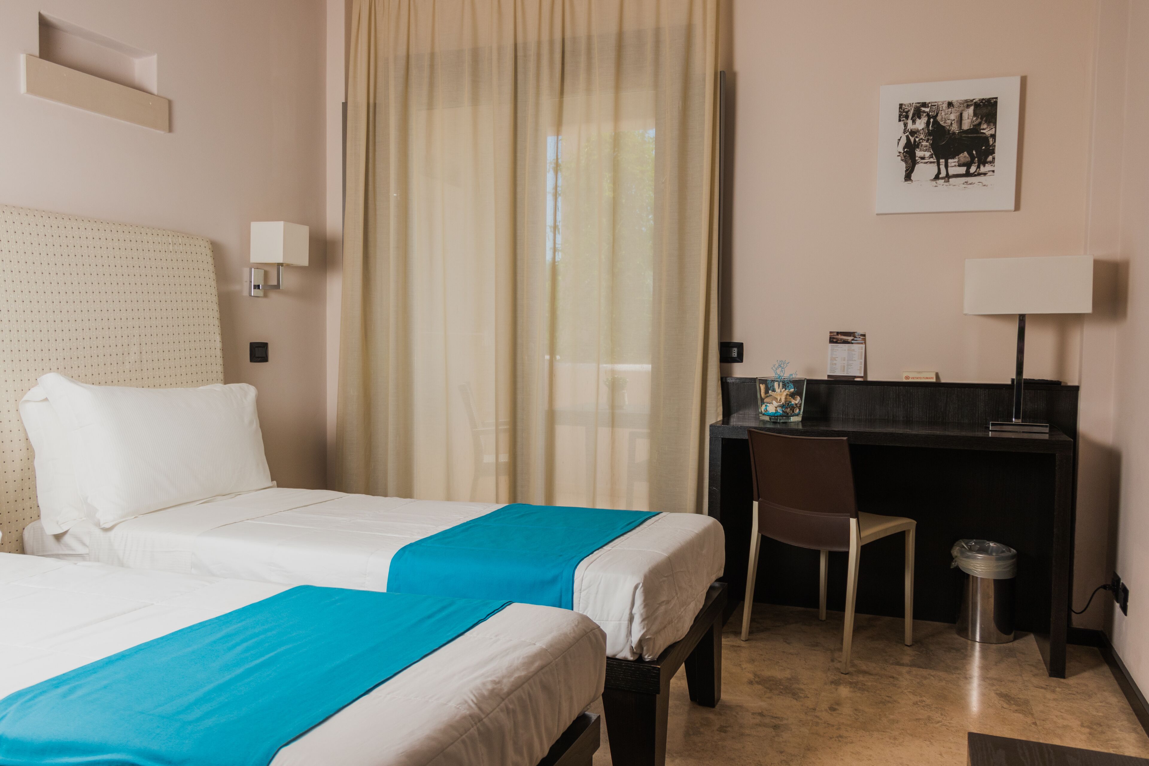 Una habitación de hotel con dos camas, un escritorio, una silla y un bote de basura.