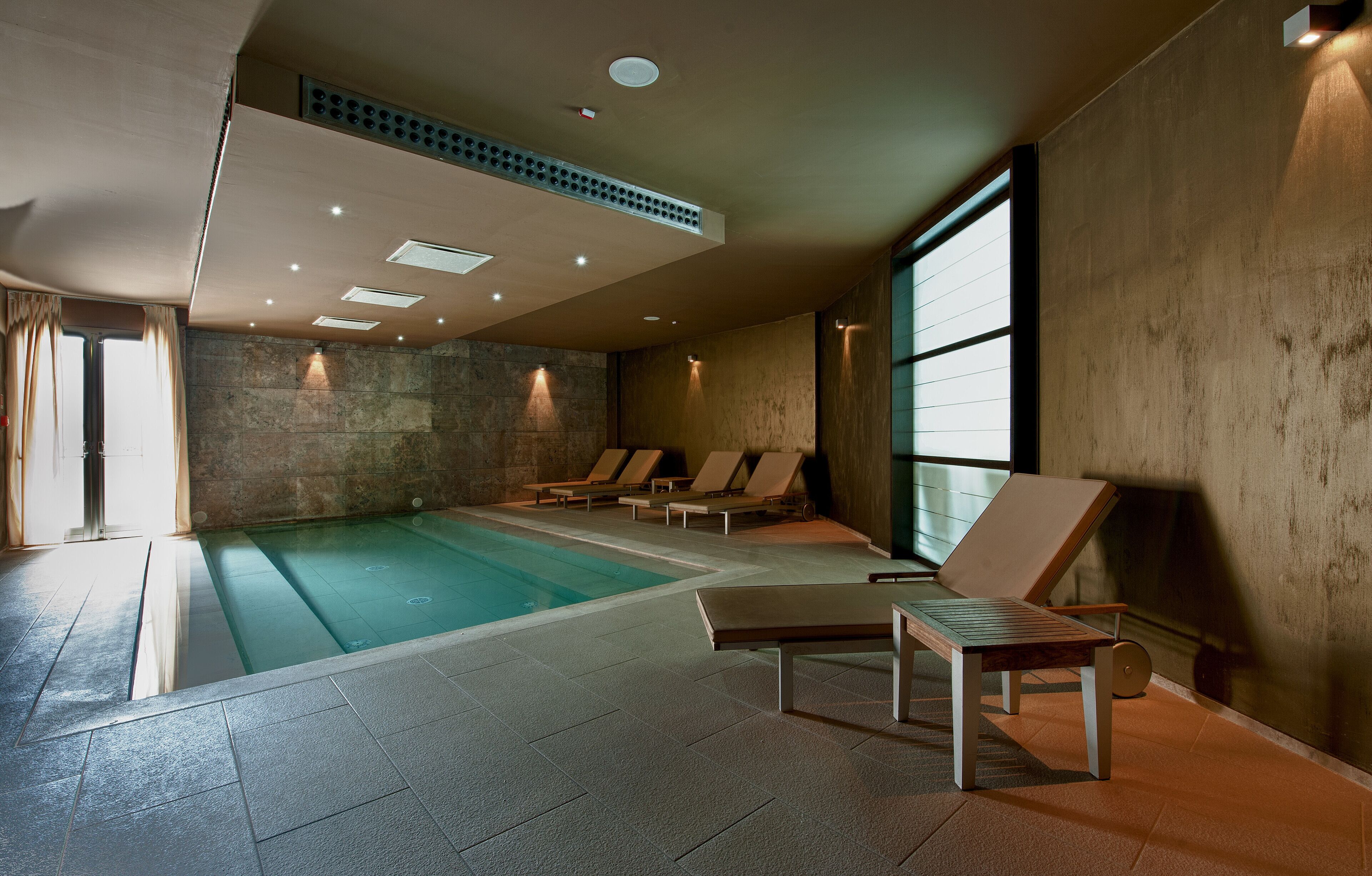 Una piscina interior con sillas de descanso y una pared de piedra.