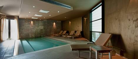 Una piscina interior con sillas de descanso y una pared de piedra.