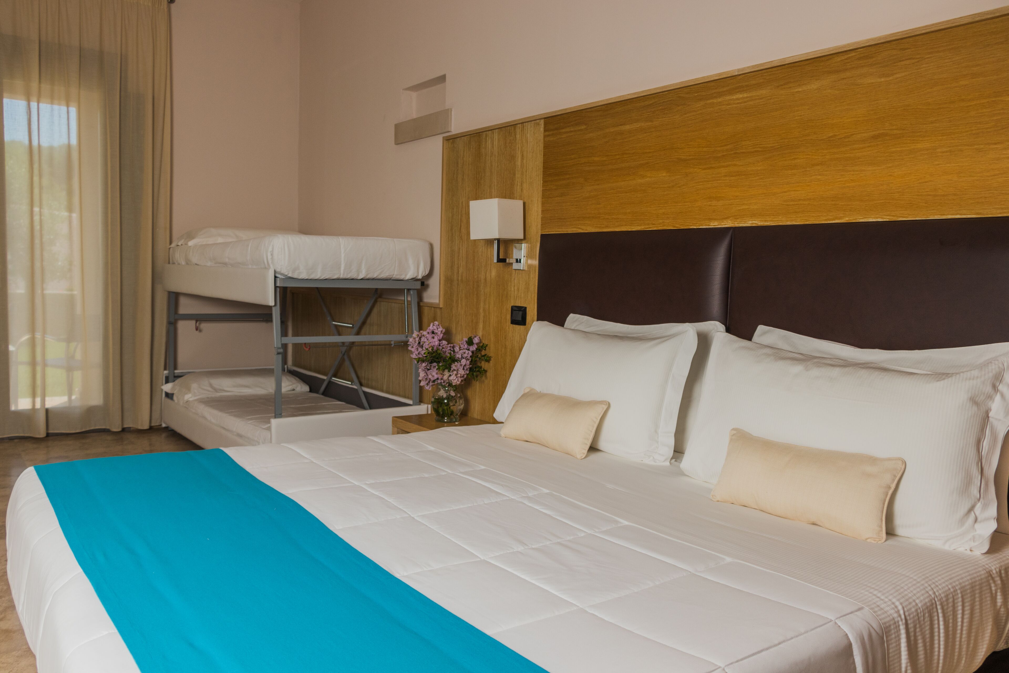 Ein Hotelzimmer mit einem großen Bett, einem Etagenbett, einem Nachttisch mit Lampe und einem Fenster mit Vorhängen.