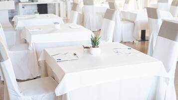 Ein Restaurant mit weißen Tischdecken und Stühlen, einer kleinen Topfpflanze auf jedem Tisch und einem klaren, modernen Interieur.