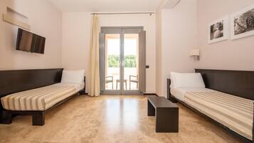 A room with two single beds, a flat-screen TV mounted on the wall, a small table, and a sliding glass door leading to an outdoor area.