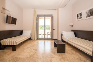 A room with two single beds, a flat-screen TV mounted on the wall, a small table, and a sliding glass door leading to an outdoor area.