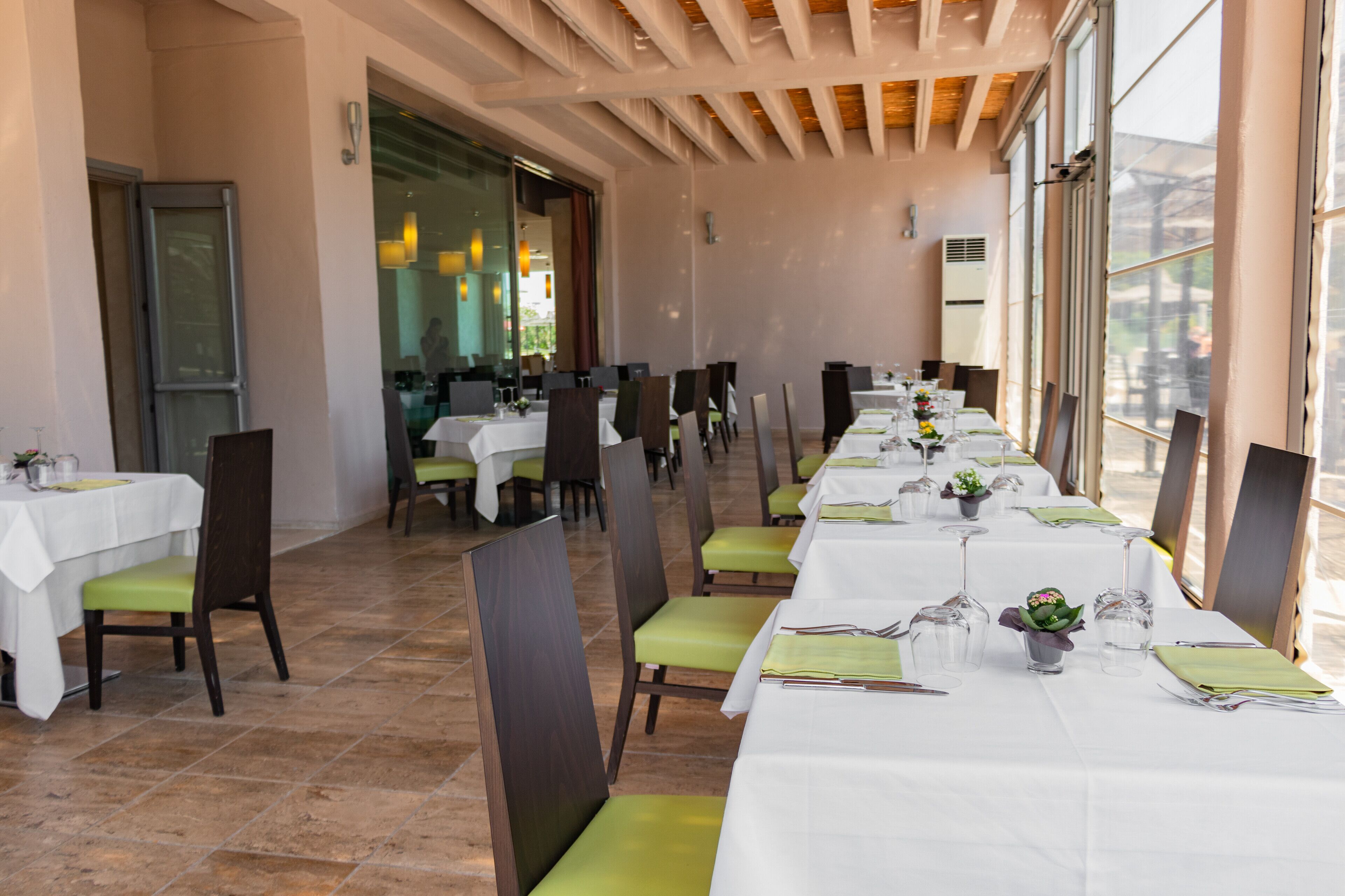 Ein Restaurant mit langen Tischen, grünen Sitzkissen und weißen Tischdecken.