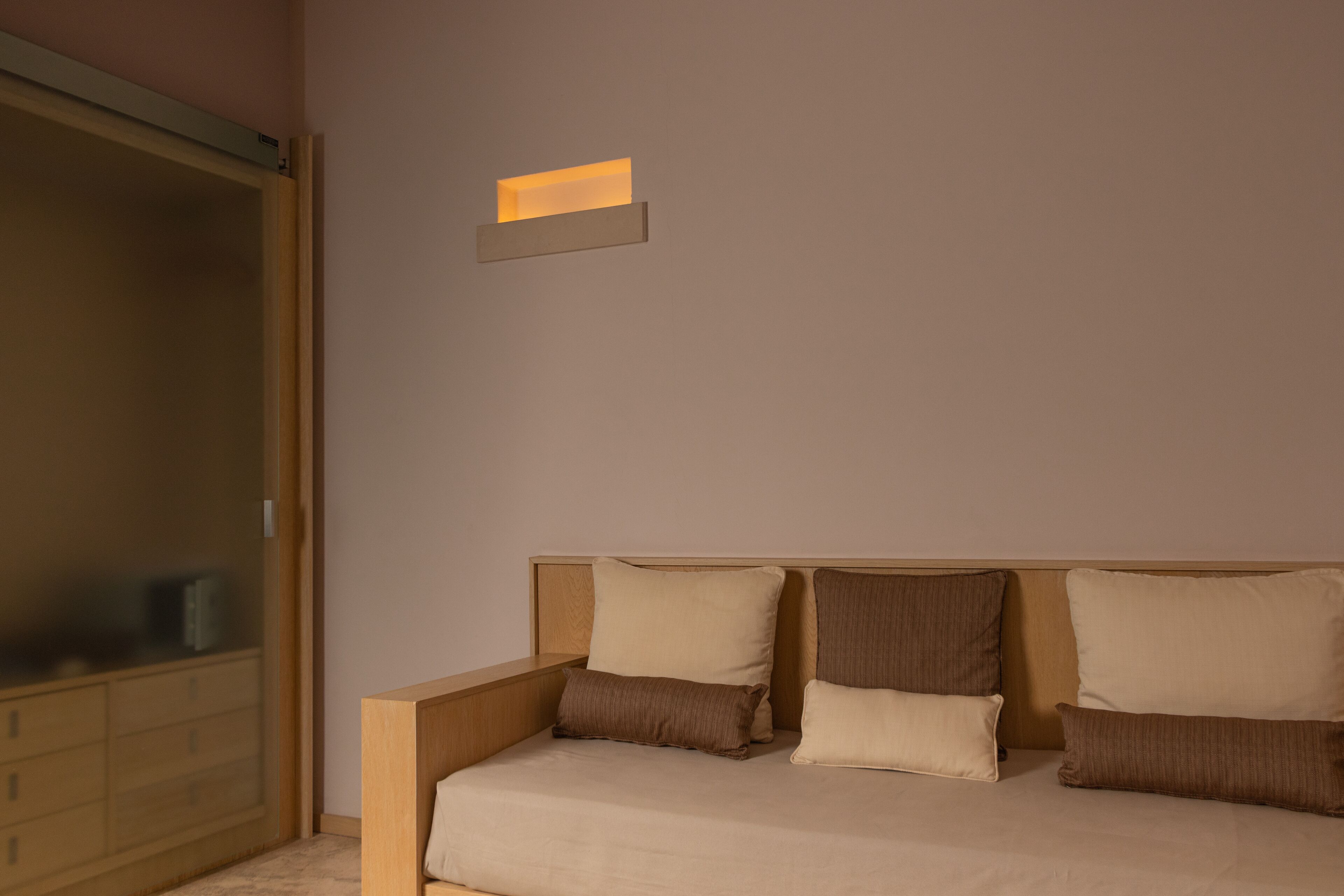 Un dormitorio con cama, almohadas, una mesita de noche y un aplique de pared.