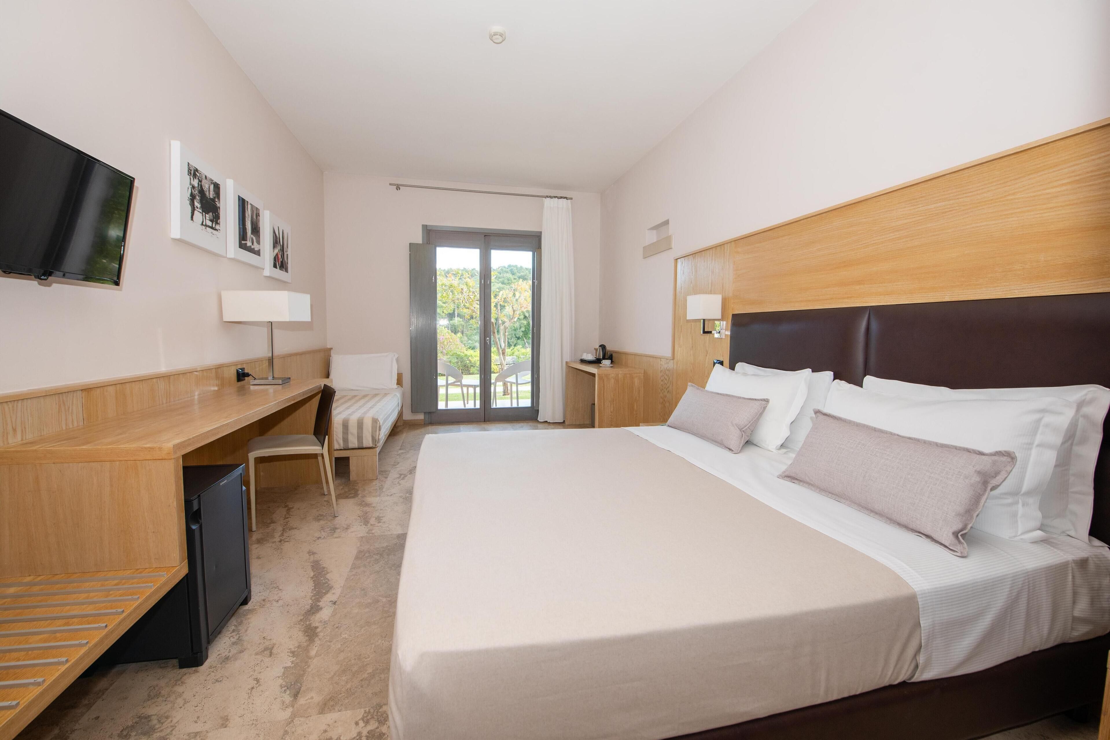 A hotel room with a bed, desk, chair, TV, and a view of the outdoors.