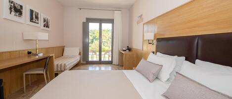 A hotel room with a large bed, a desk, a chair, and a view of the outdoors through a sliding door.