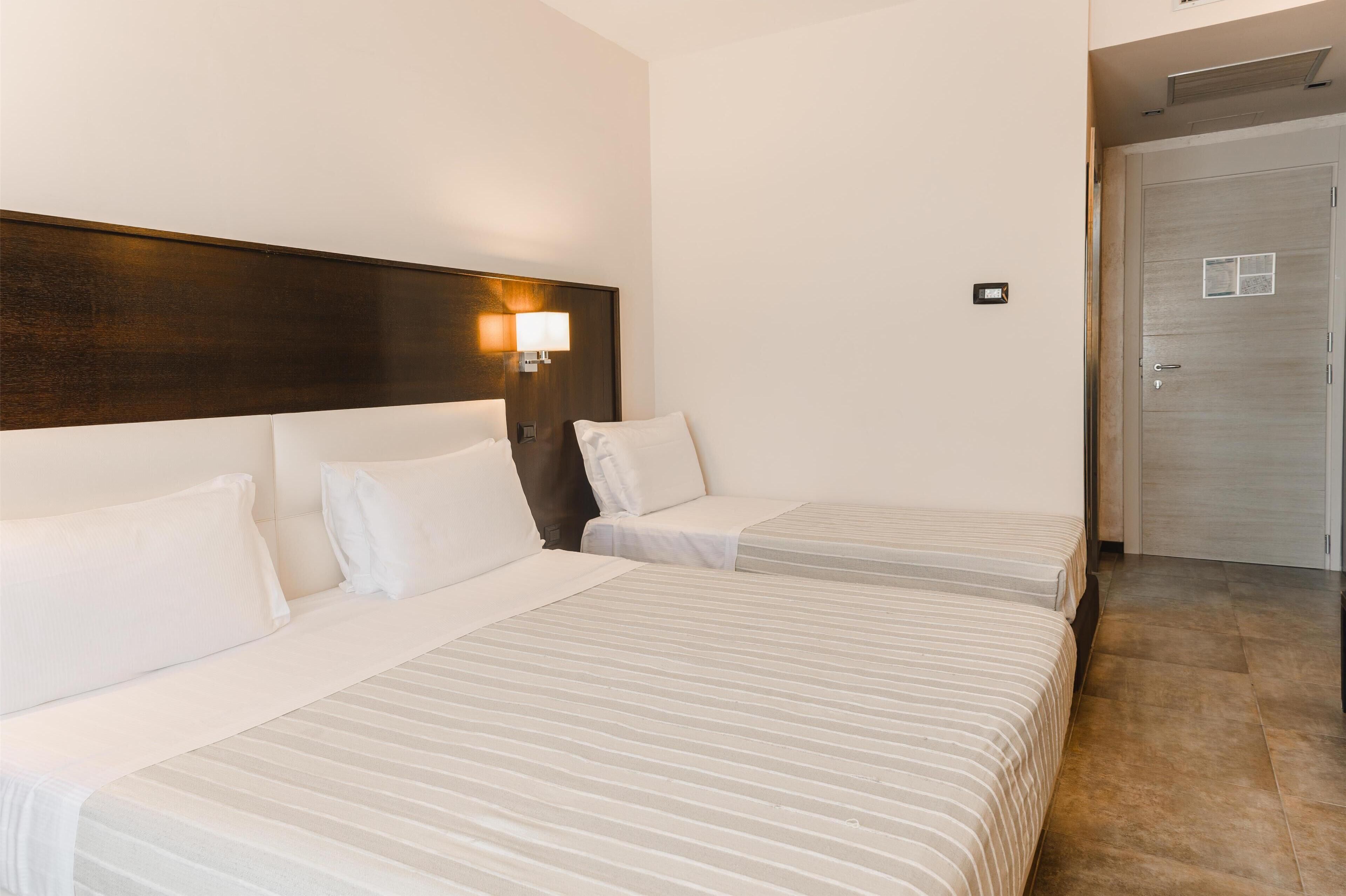 Une chambre d’hôtel avec deux lits, une tête de lit en bois, une lampe de chevet et une porte.