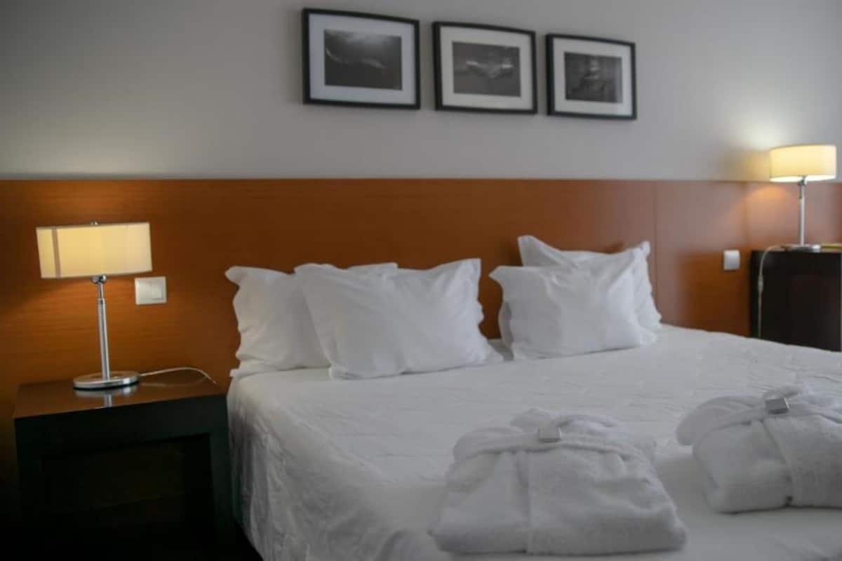 Ein Hotelzimmer mit einem großen Bett, zwei Nachttischlampen, einem Schreibtisch mit Stuhl und drei gerahmten Bildern an der Wand.