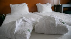A hotel room with a neatly made bed, two white towels with green embroidery, and a wooden headboard. - Inatel Flores Hotel (Santa Cruz das Flores)