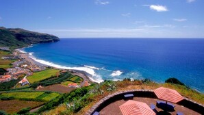 A coastal view with a beach, ocean, and a circular seating area with umbrellas. - Inatel Flores Hotel (Santa Cruz das Flores)