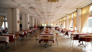 Une grande salle à manger avec de nombreuses tables et chaises disposées en rangées, de hauts plafonds et de grandes fenêtres.
