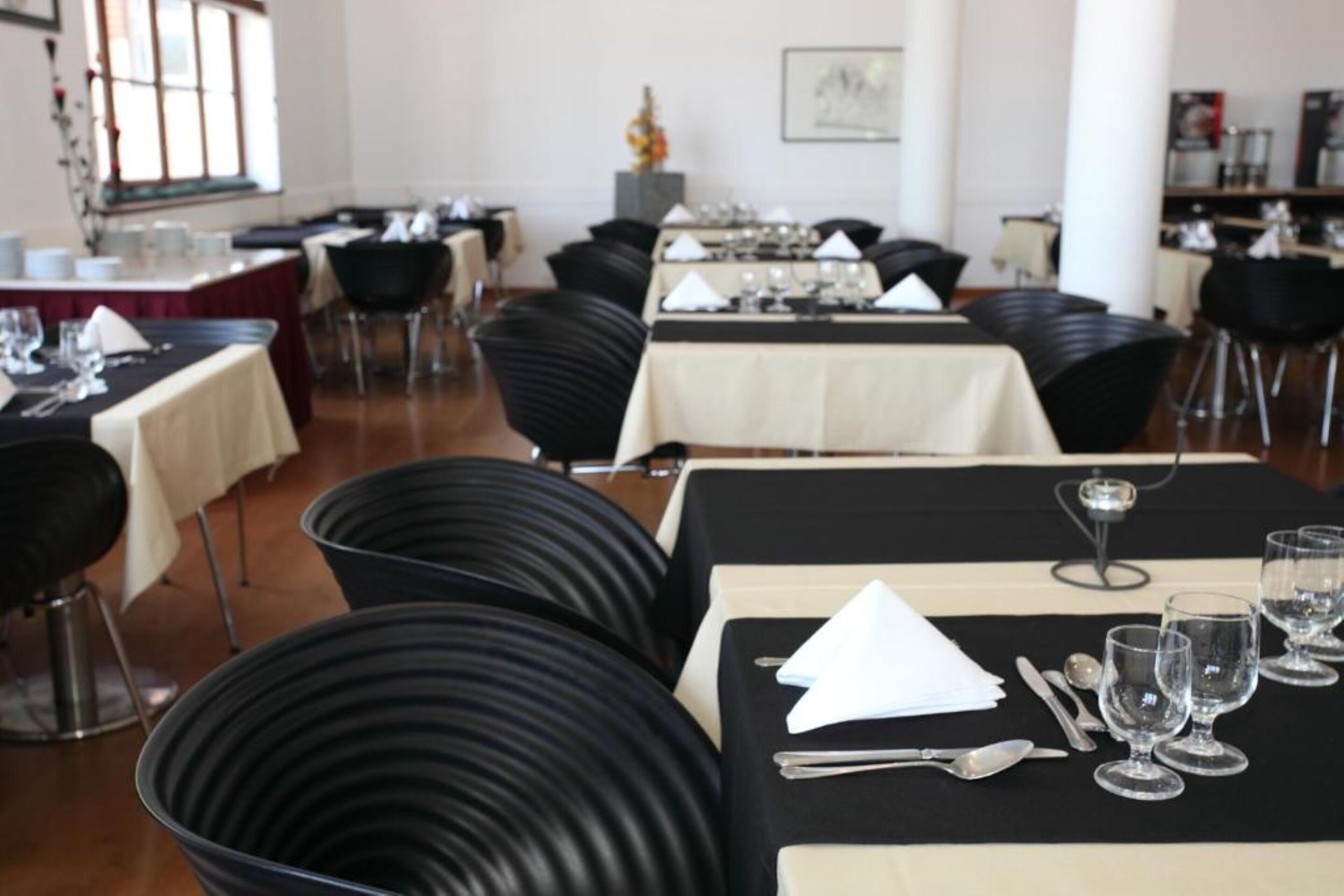 Comedor con varias mesas dispuestas para el servicio, sillas negras y una paleta de colores neutros.