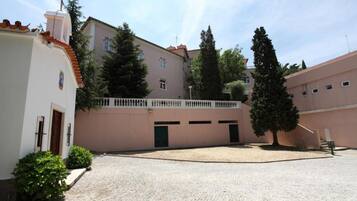 Um pátio com pavimento de pedra, um edifício branco com uma porta verde, e um edifício rosa com varanda.